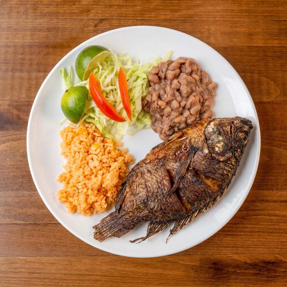 Fried whole fish with rice, beans, shredded lettuce, lime wedges, and red pepper slices.