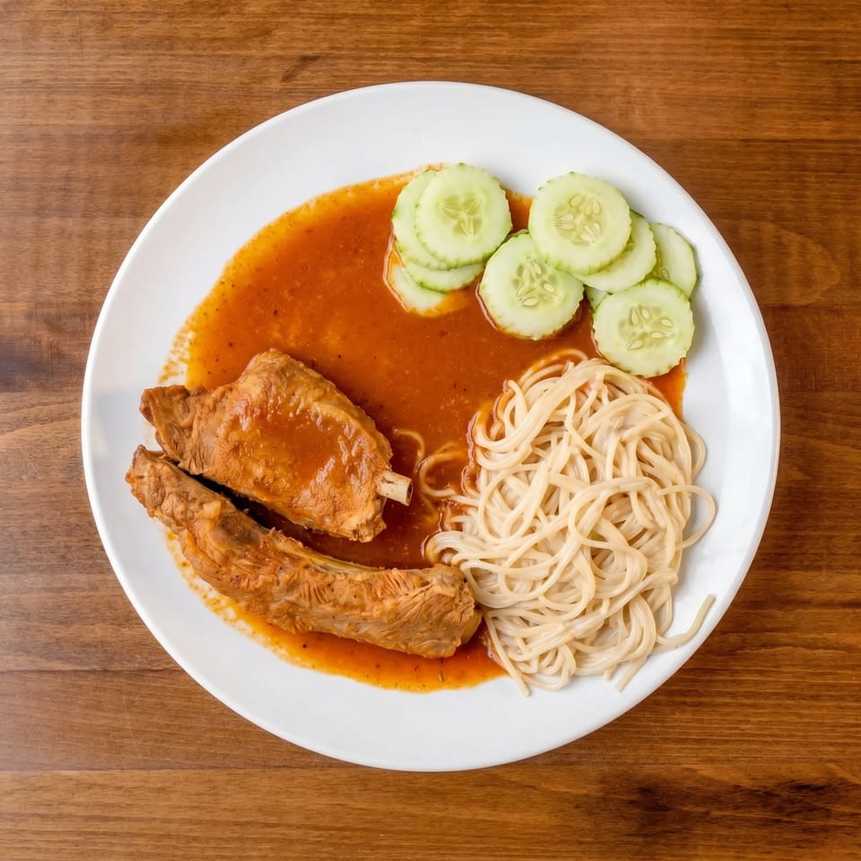 Two ribs in red sauce with spaghetti and cucumber slices on a white plate.