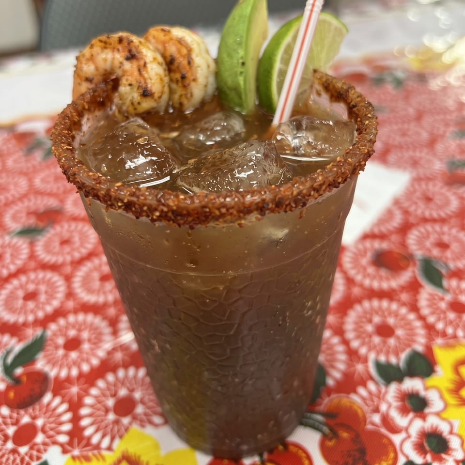 Spicy shrimp cocktail with avocado and lime slices, served in a chili-rimmed glass.