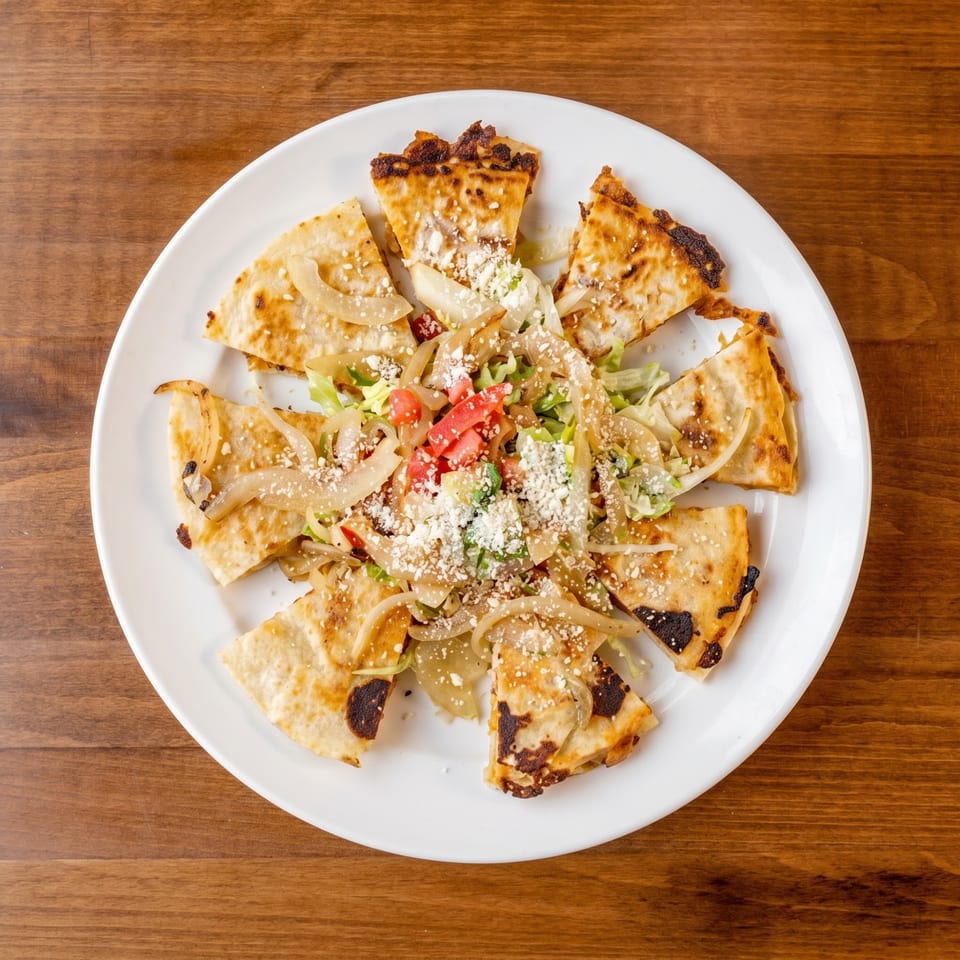Overhead view of a white plate with quesadilla slices, topped with onions, lettuce, tomatoes, and cheese.